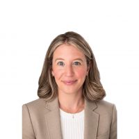 Professional headshot of a smiling woman in a beige blazer and white blouse