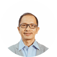 Professional headshot of a smiling man wearing glasses, a light blue shirt, and a gray blazer, against a white circular background with a green edge.