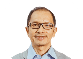 Professional headshot of a smiling man wearing glasses, a light blue shirt, and a gray blazer, against a white circular background with a green edge.